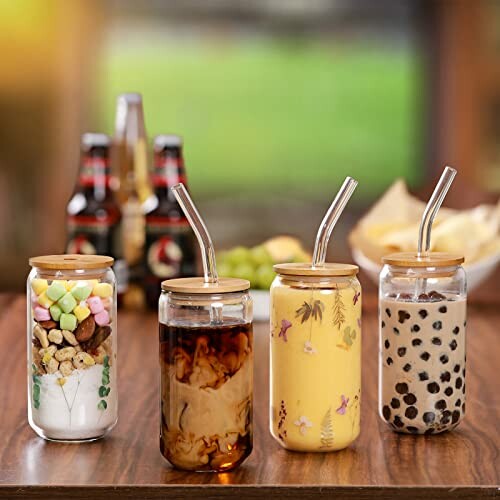 Four glass jars with drinks and straws on a wooden table.