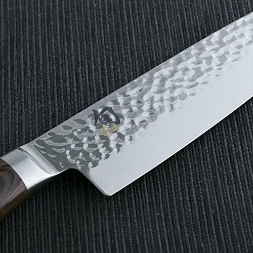 Close-up of a chef's knife with a textured blade on a dark surface.