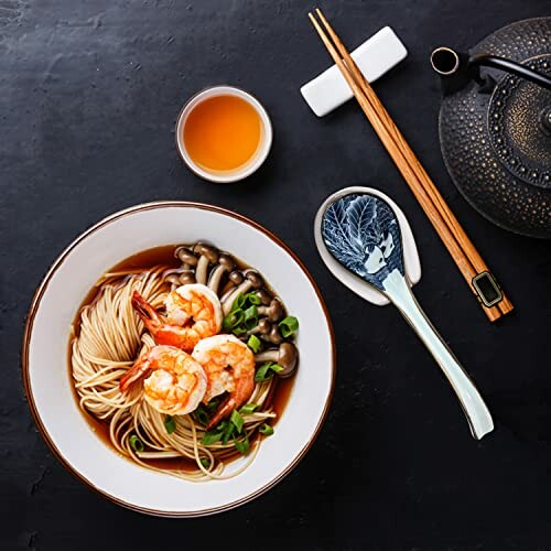 Bowl of noodle soup with shrimp, mushrooms, and green onions, accompanied by tea, chopsticks, and teapot.