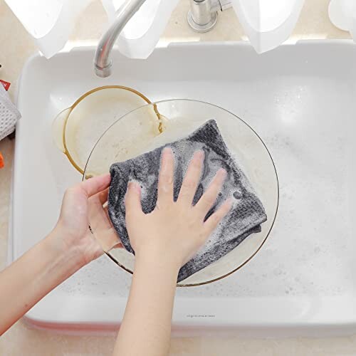 Hands washing a plate with soapy water in a sink